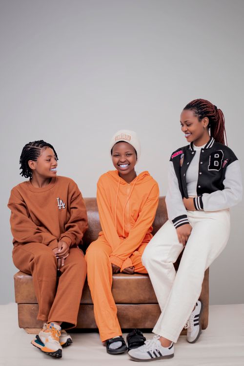 Free Three friends dressed in casual outfits, smiling and sitting indoors on a couch. Stock Photo