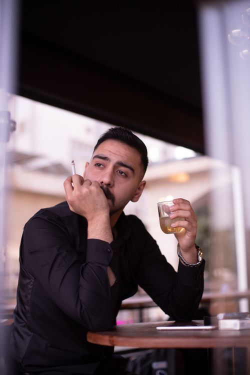 Free Man relaxing indoors with a drink and cigarette in a Cairo café, exuding a thoughtful mood. Stock Photo