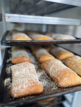 Multiple ciabatta loaves cooling on a rack in a bakery, dusted with flour.
