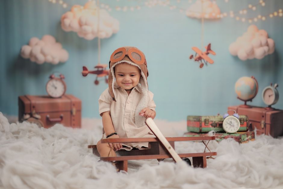 Charming young child in aviator gear surrounded by whimsical clouds and vintage travel decor.