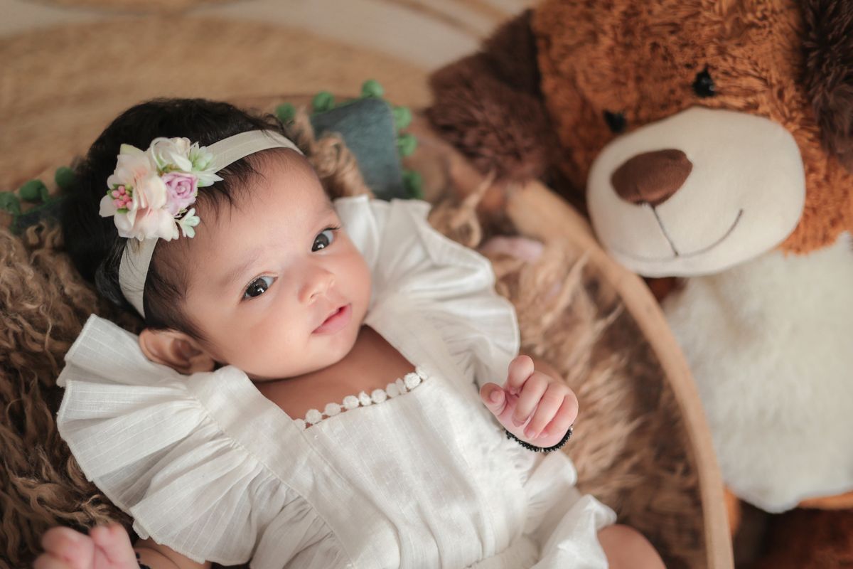 Baby with a floral headband and teddy bear