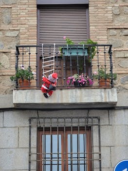 A humorous scene of Santa climbing a balcony with flowers in Toledo, Spain.