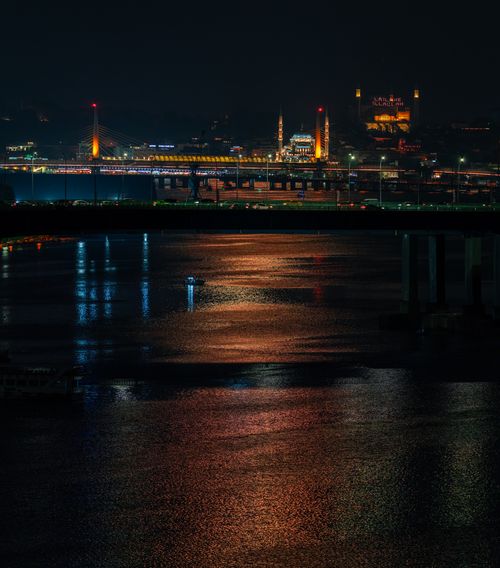 Free Stunning night view of a lit-up bridge with city lights reflecting on a river. Stock Photo