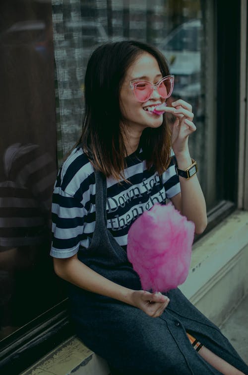 Woman Sitting near Glass Wall Eating Cotton Candy 