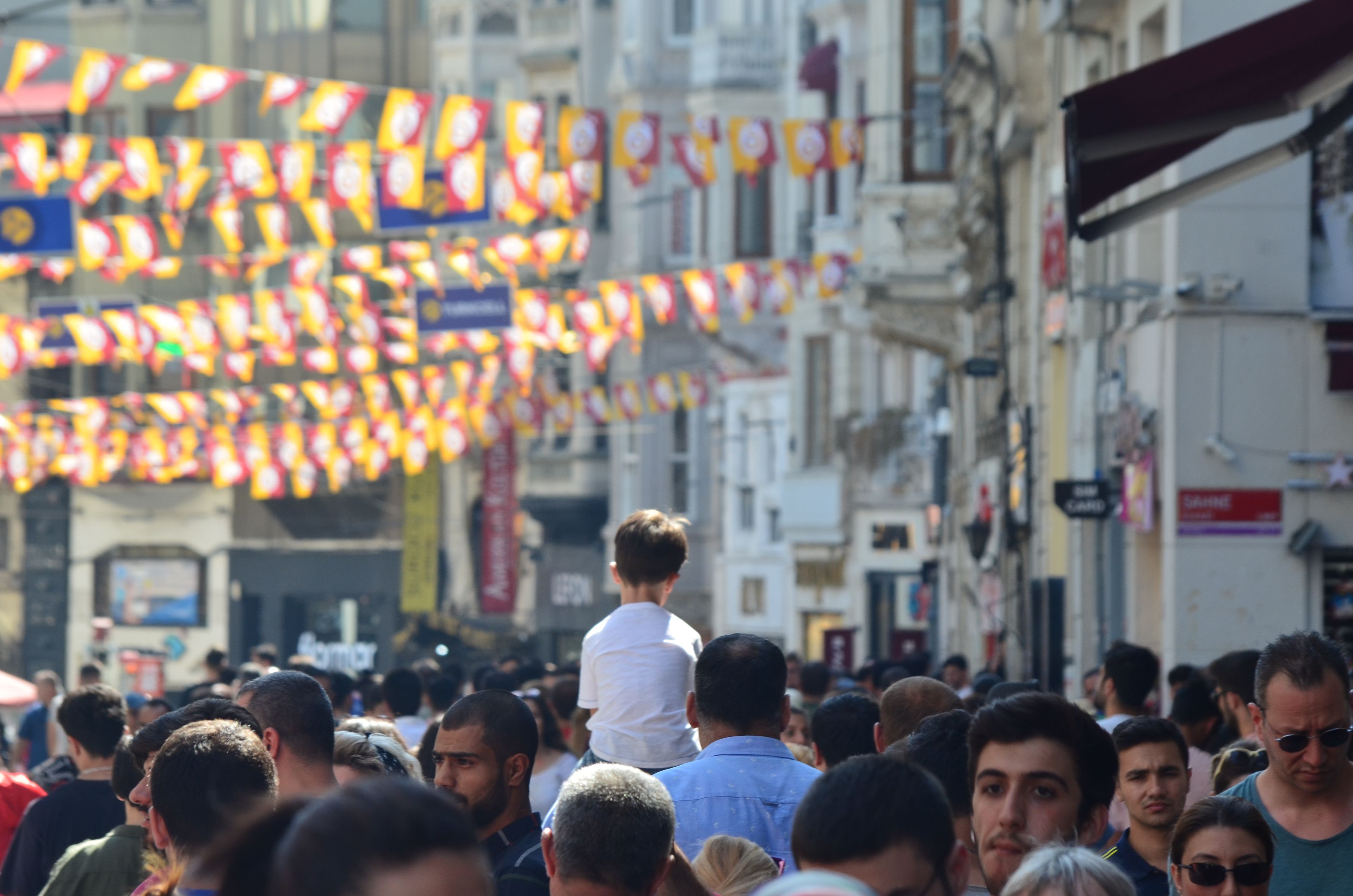 A bustling street scene filled with colorful flags and a crowd in daylight.