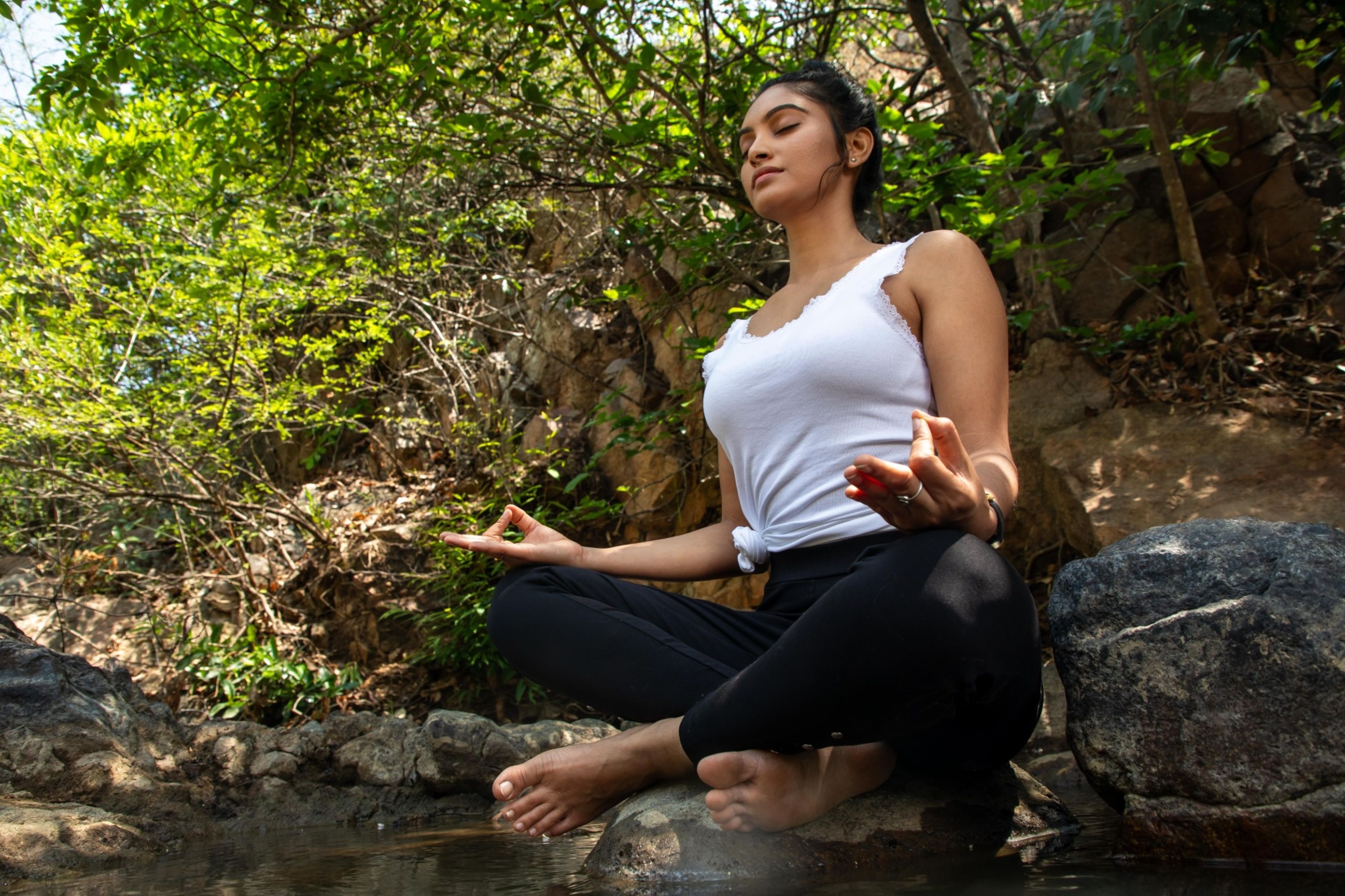 A woman meditating peacefully beside a forest stream, reflecting the relational and somatic nature of MDMA integration practice.