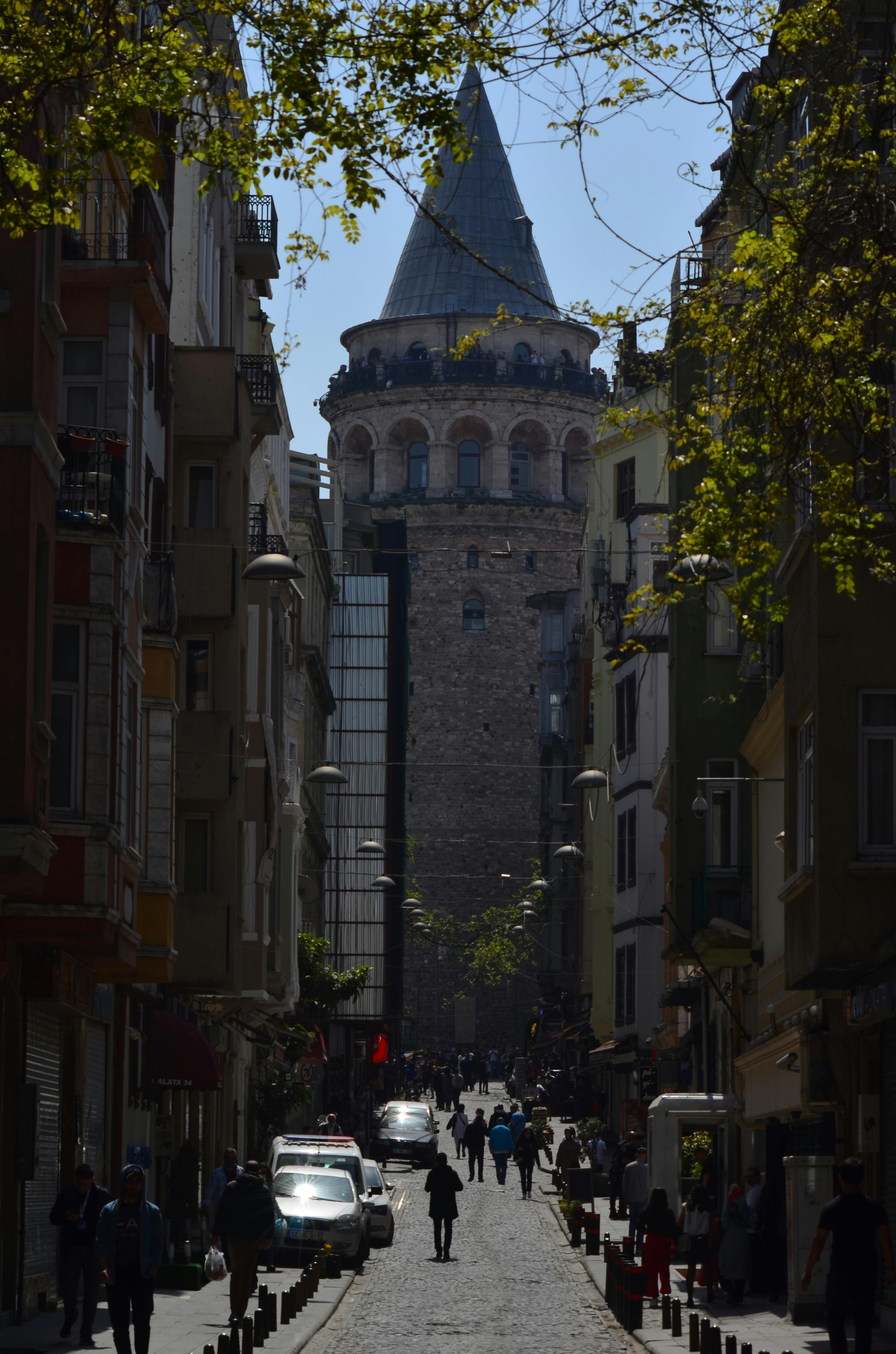 A bustling street scene leading to the historic Galata Tower in Istanbul.