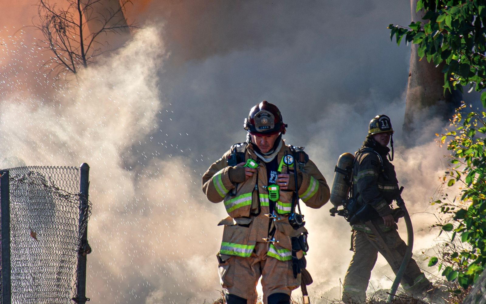 Firefighters in protective gear working to extinguish a forest fire amid heavy smoke