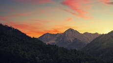 山区景观中，充满活力的天空与郁郁葱葱的森林映衬着令人惊叹的日落