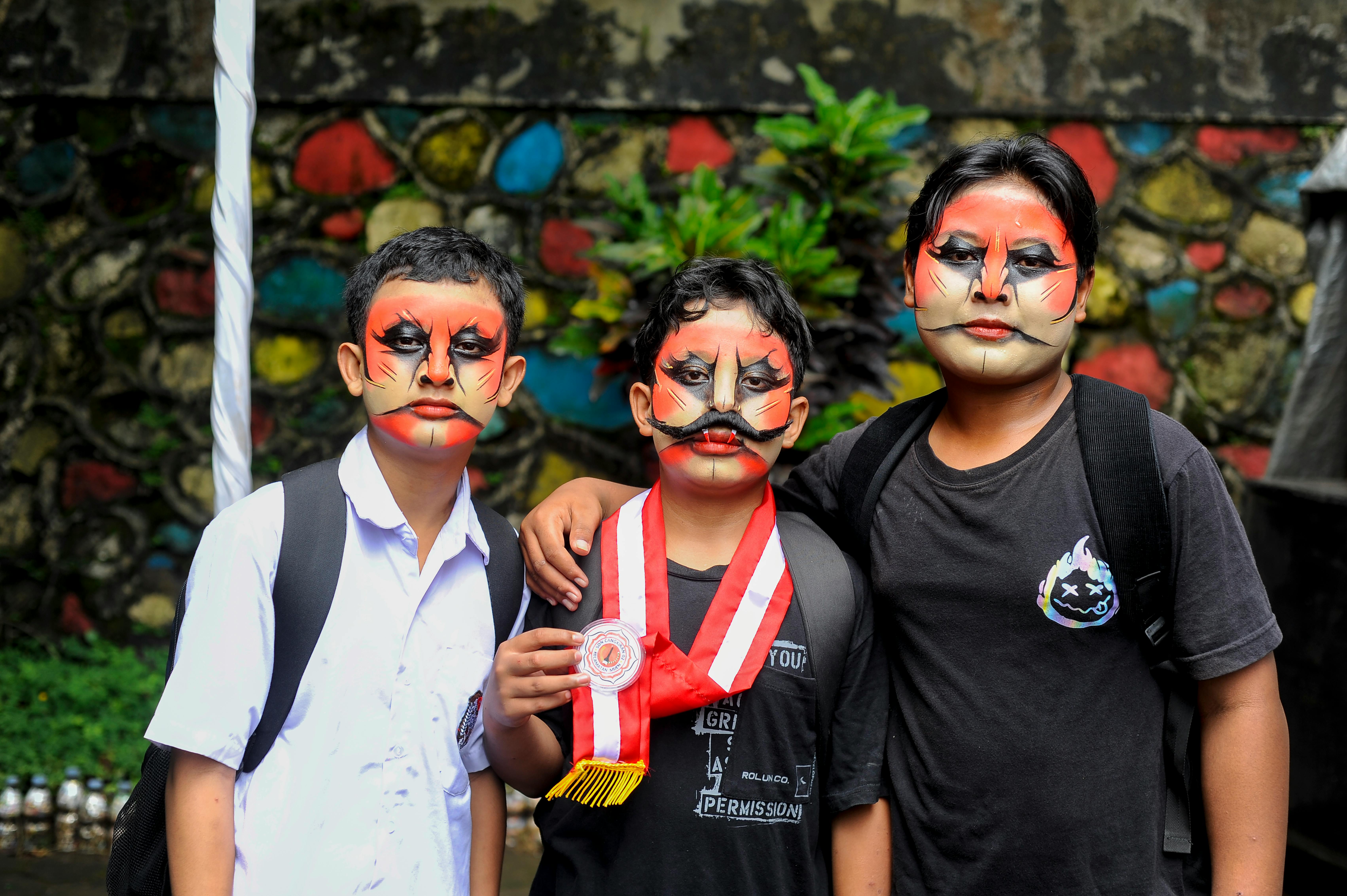 grátis Três garotos com maquiagem teatral dramática e uma medalha em pé ao ar livre, perto de uma parede colorida. Foto profissional