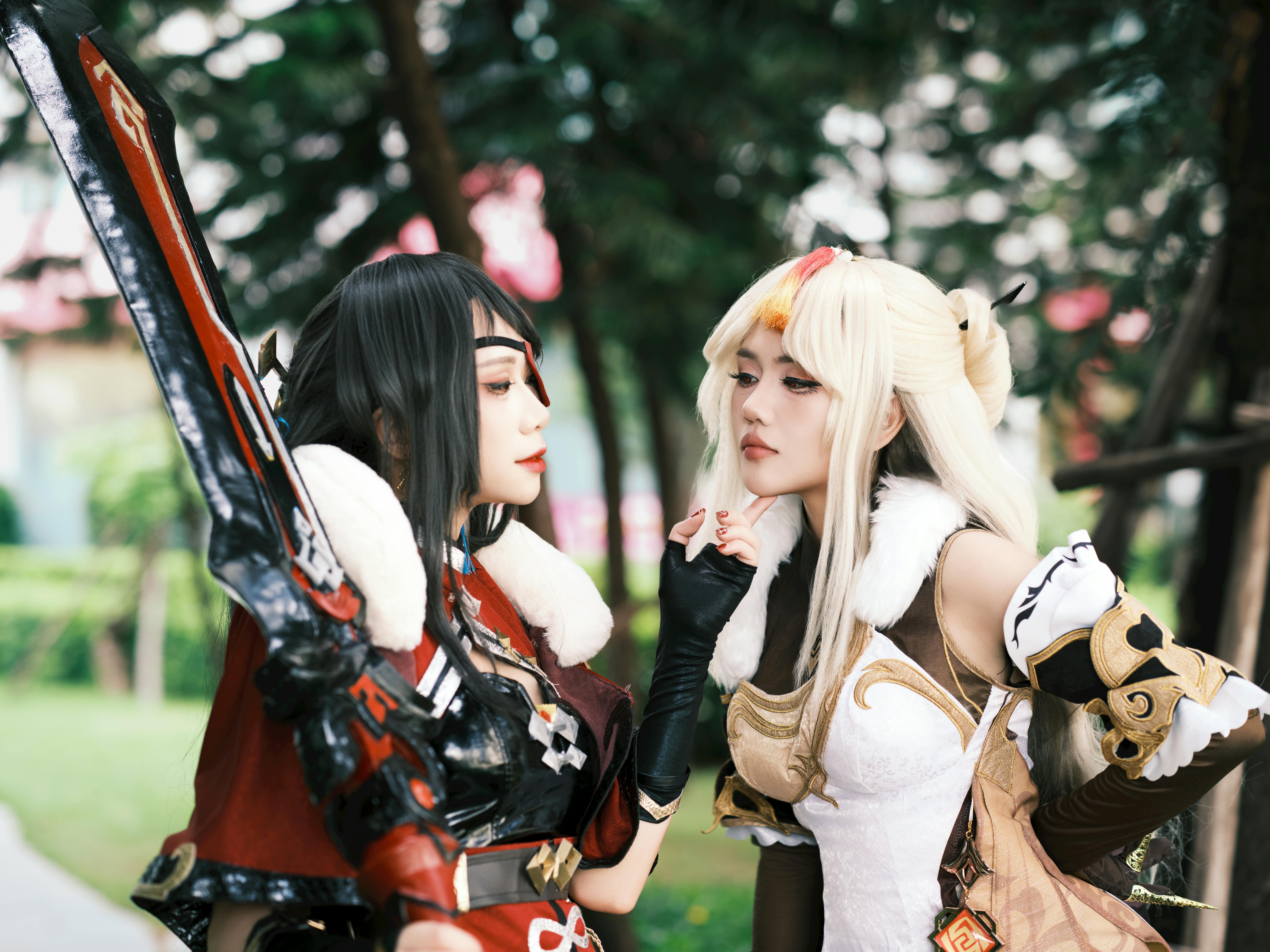 Two adults in elaborate fantasy cosplay costumes engage outdoors, surrounded by greenery.
