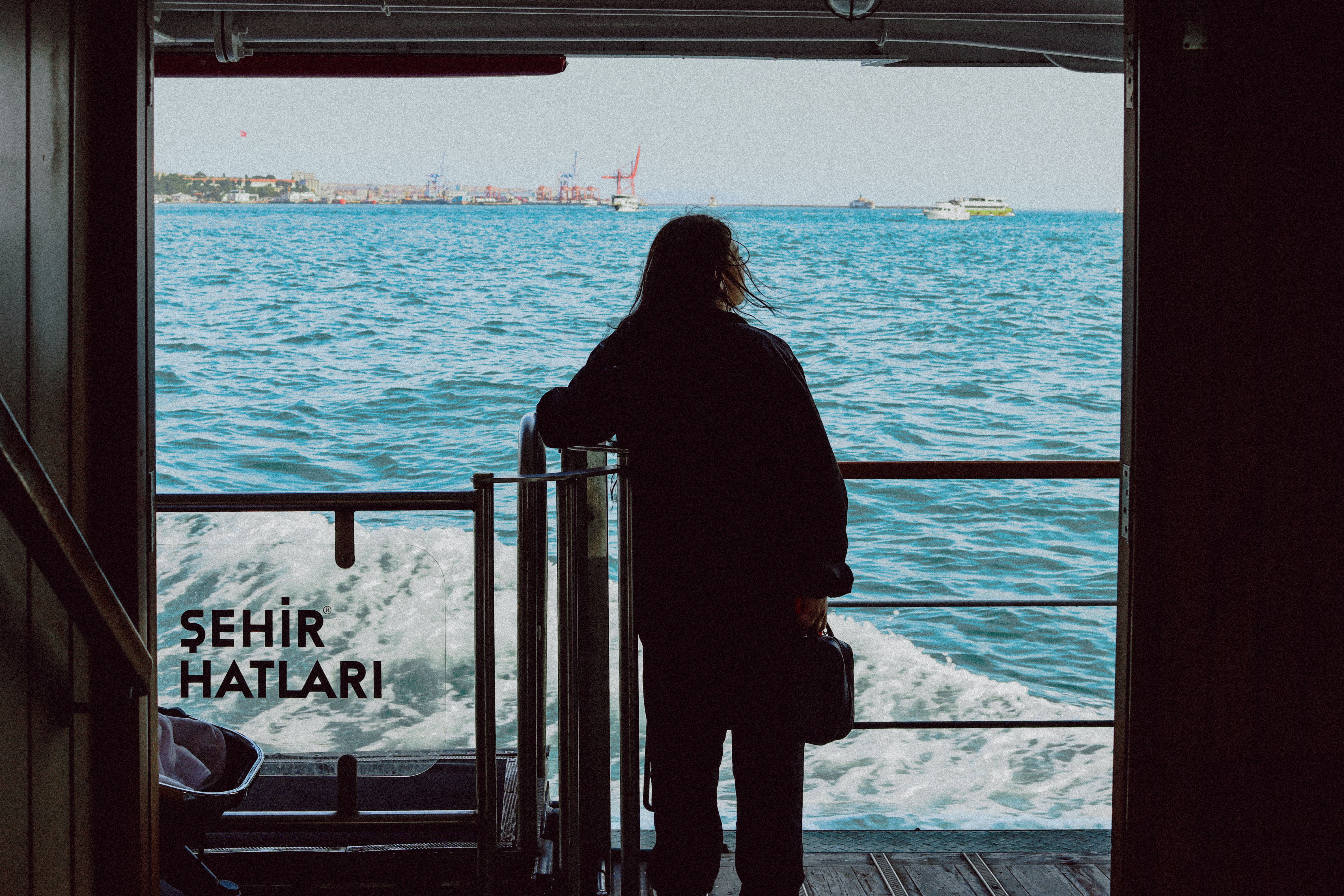 Silhouette of person on ferry with ocean view, capturing serene travel vibe in daylight.