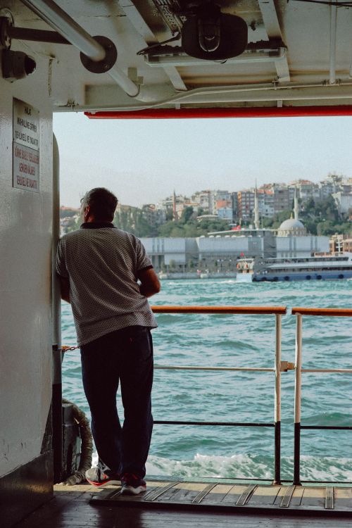 Free A man stands on a ferry in Istanbul, gazing at the city's cityscape and waterfront. Stock Photo
