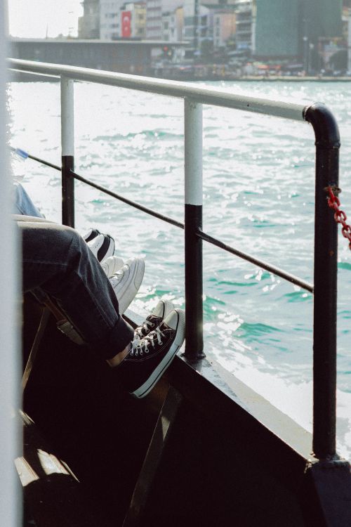 Free Casual sneakers hanging off a boat rail enjoying a sunny waterfront city skyline. Stock Photo