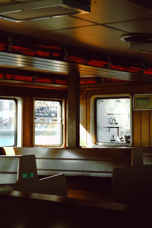 Free Warm sunlight casts shadows in an empty ferry interior with wood paneling and benches. Stock Photo