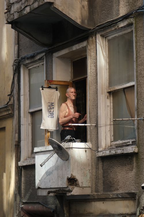 Free An elderly man looks out from a rustic apartment window on a sunny day. Stock Photo