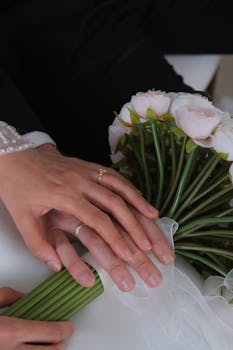 Close-up of couple's hands with wedding rings and rose bouquet, symbolizing love.