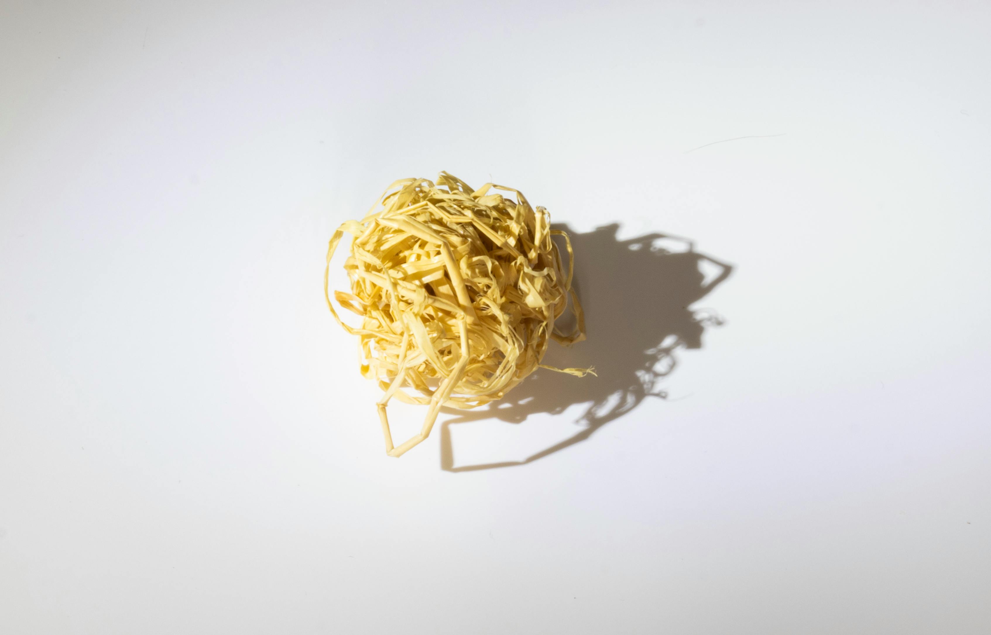 A ball of tangled raffia on a white background casting an intricate shadow. Perfect for design projects.