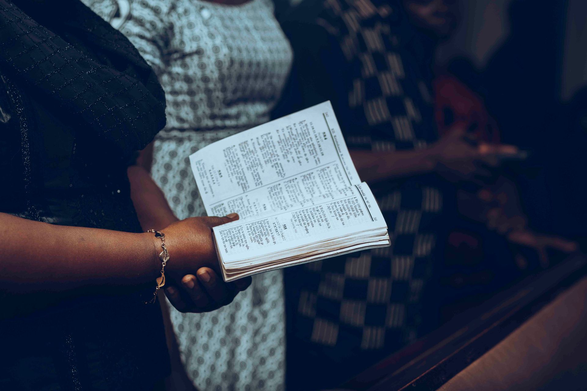 Close-up of a diverse congregation holding a hymn book during a religious service indoors.