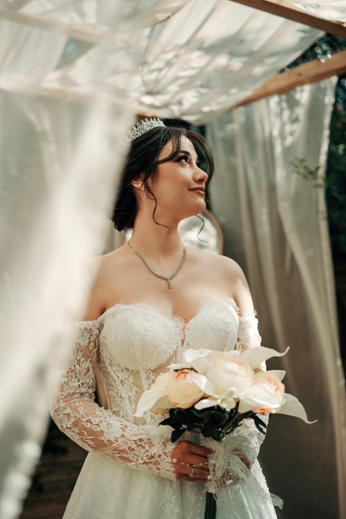 Free Beautiful bride in lace gown holding bouquet under soft daylight, exuding elegance and serenity. Stock Photo