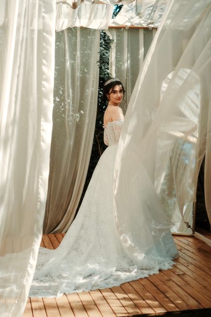 Bride in lace gown posing outdoors surrounded by flowing curtains and soft sunlight.