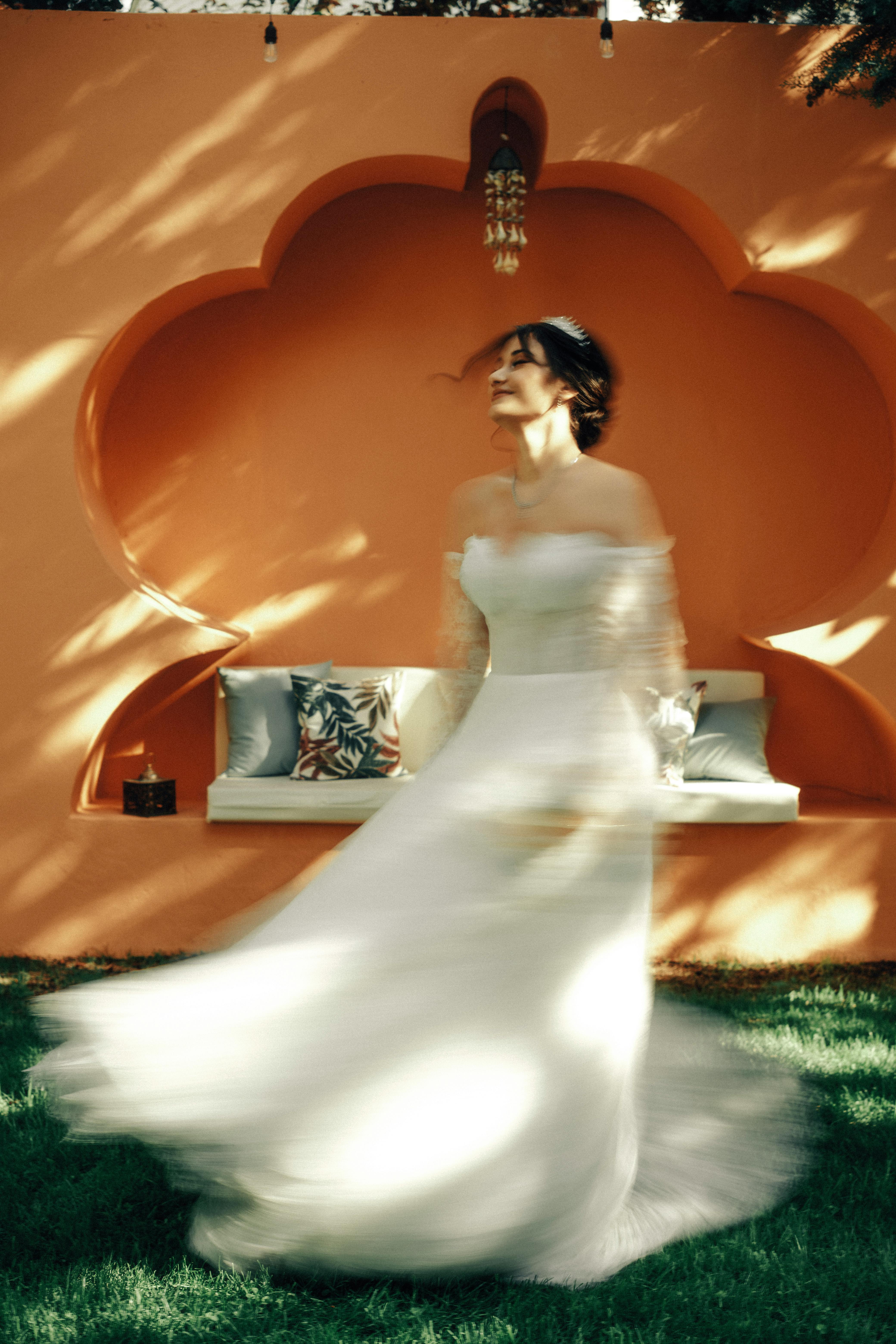 Blurred bride twirls gracefully outdoors in front of Moroccan-style wall.