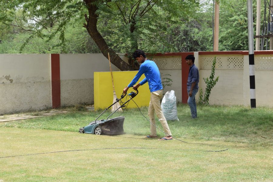 Young men working together on lawn maintenance with a mower in a sunny garden setting.