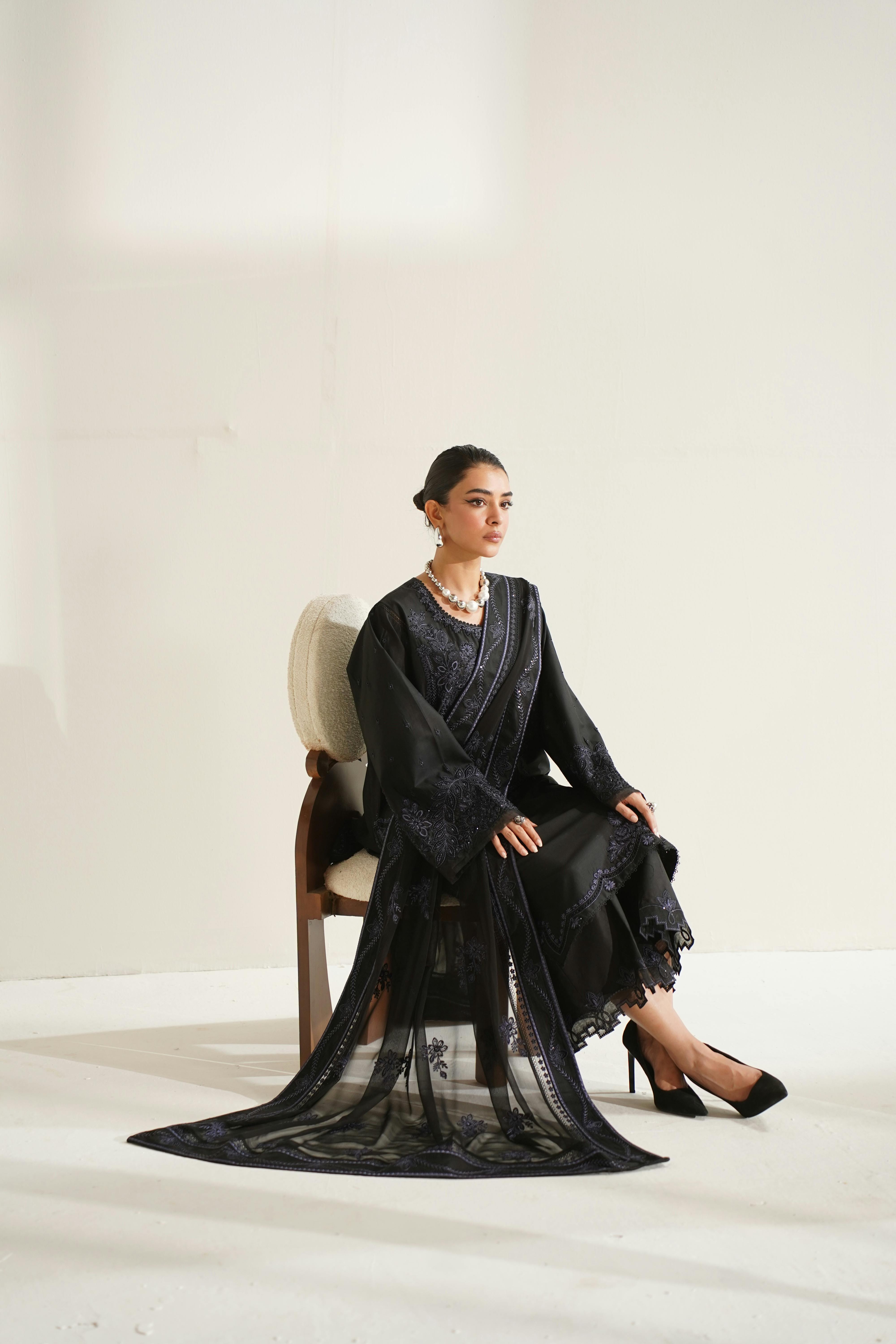Stylish black dress featuring intricate embroidery on a seated model in Lahore, Pakistan.