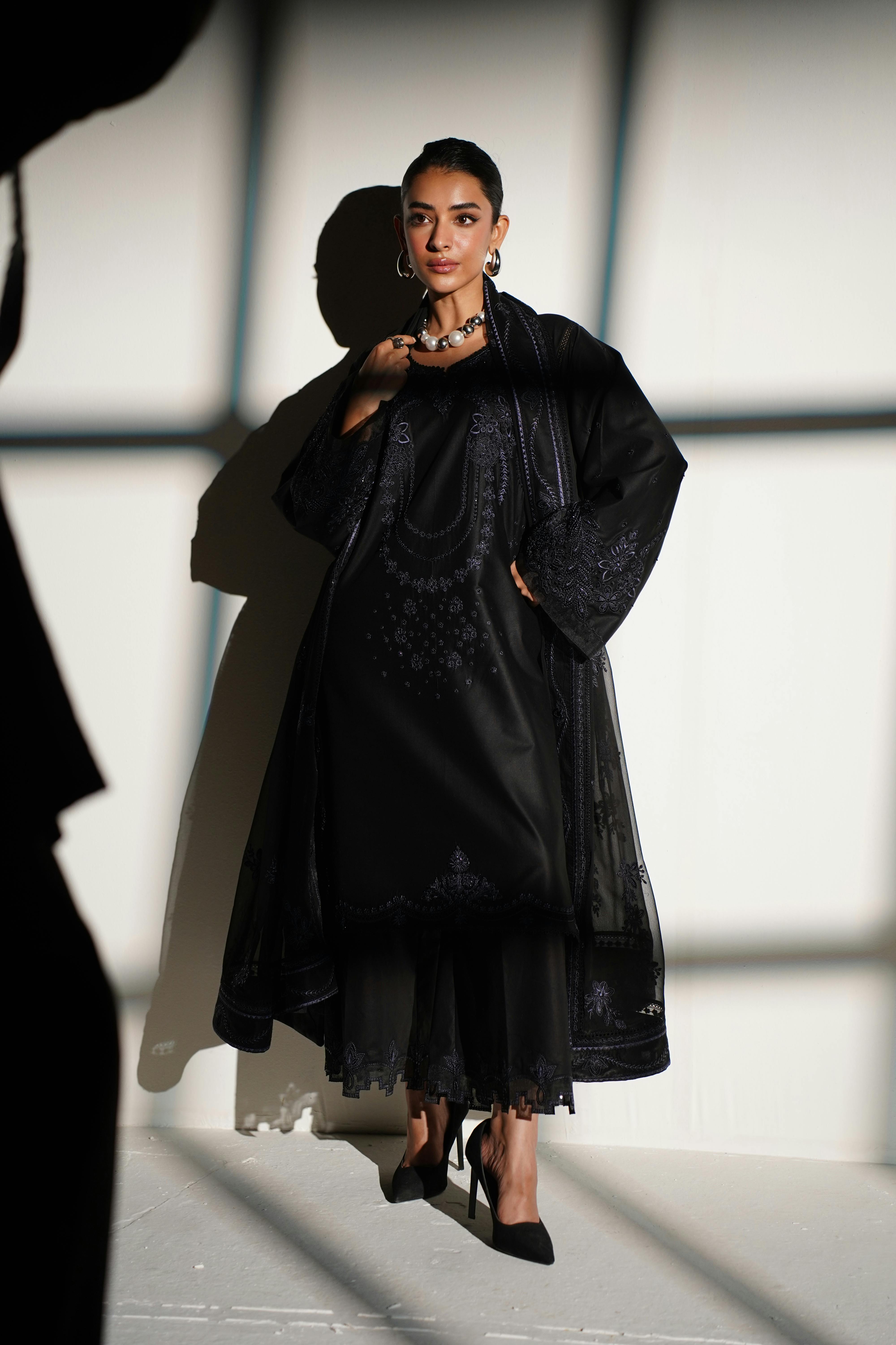 Stunning black embroidered dress in a fashion shoot against a textured background in Lahore.