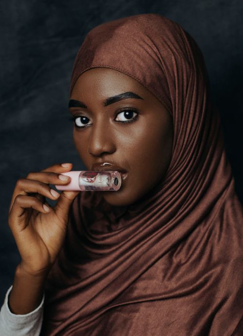 Free Portrait of a woman wearing a hijab holding lipstick against a dark background. Stock Photo