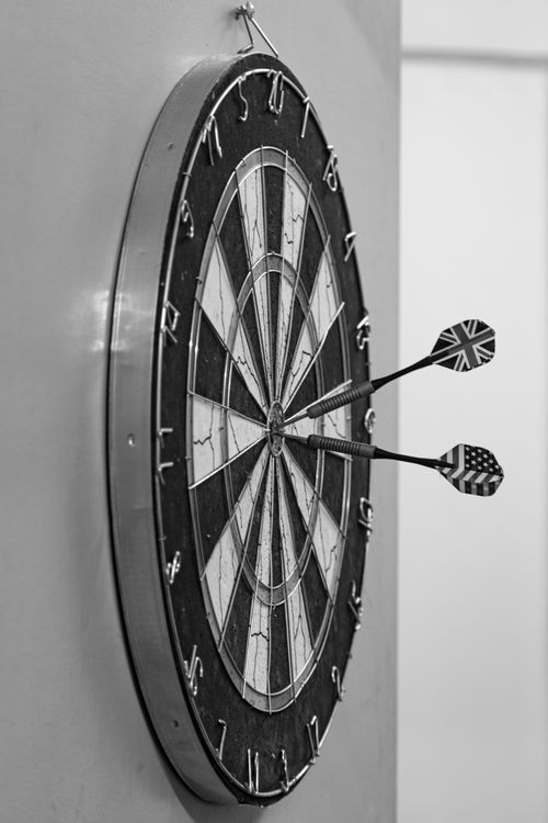 Free A monochrome side view of a dartboard with three darts, including UK and US flags. Stock Photo