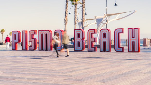 People strolling past the iconic Pismo Beach sign on a sunny day.