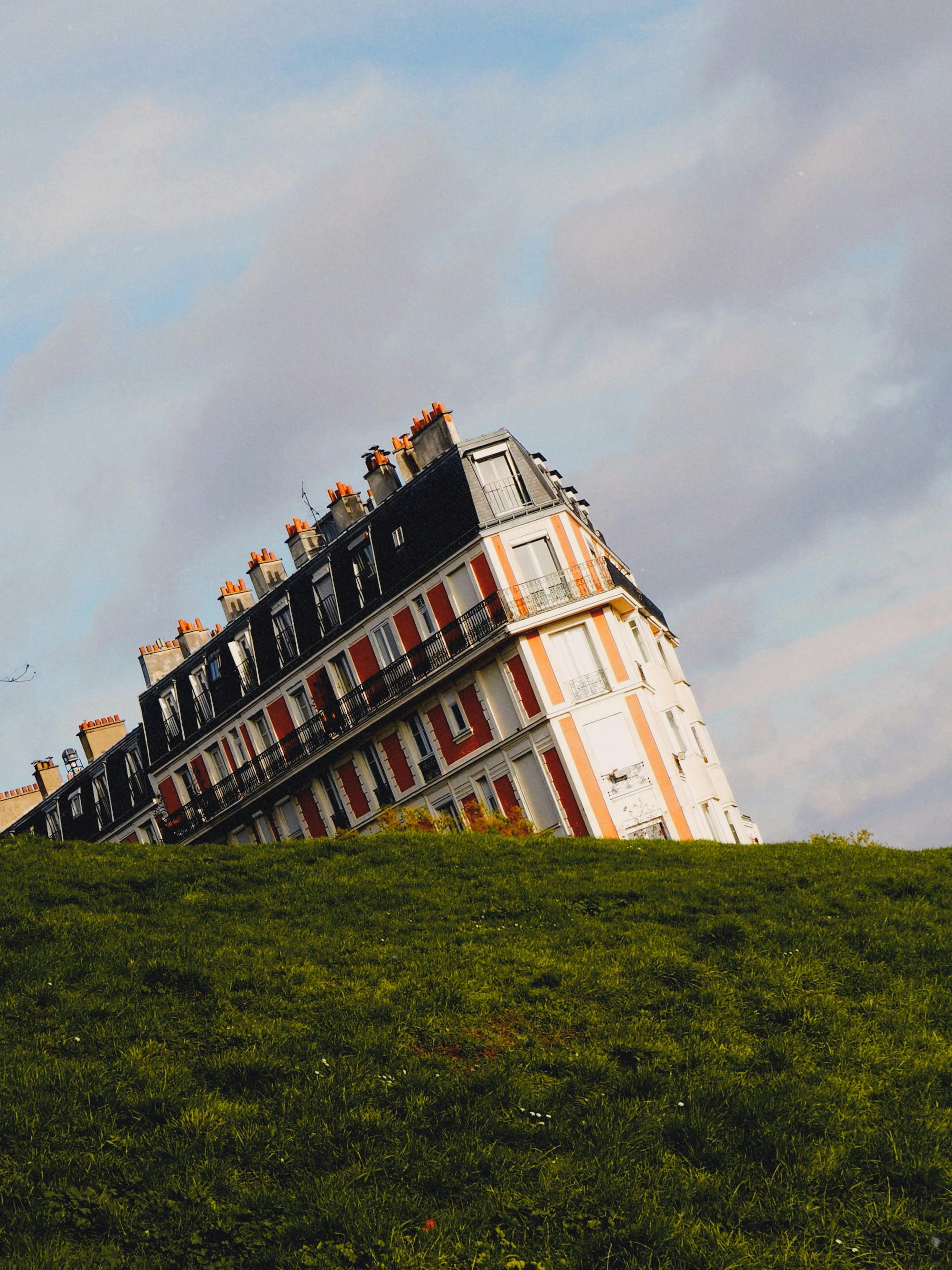 Scenic view of a tilted building in Montmartre, Paris, with green grass and a cloudy sky.