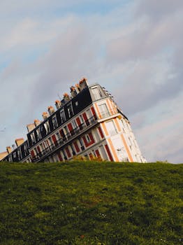 Scenic view of a tilted building in Montmartre, Paris, with green grass and a cloudy sky.