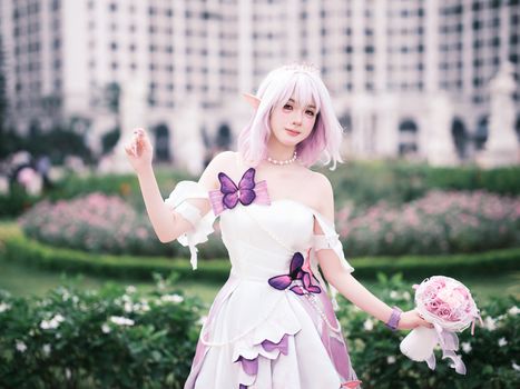 Cosplayer dressed as a fairy character posing in a lush garden with pink flowers.