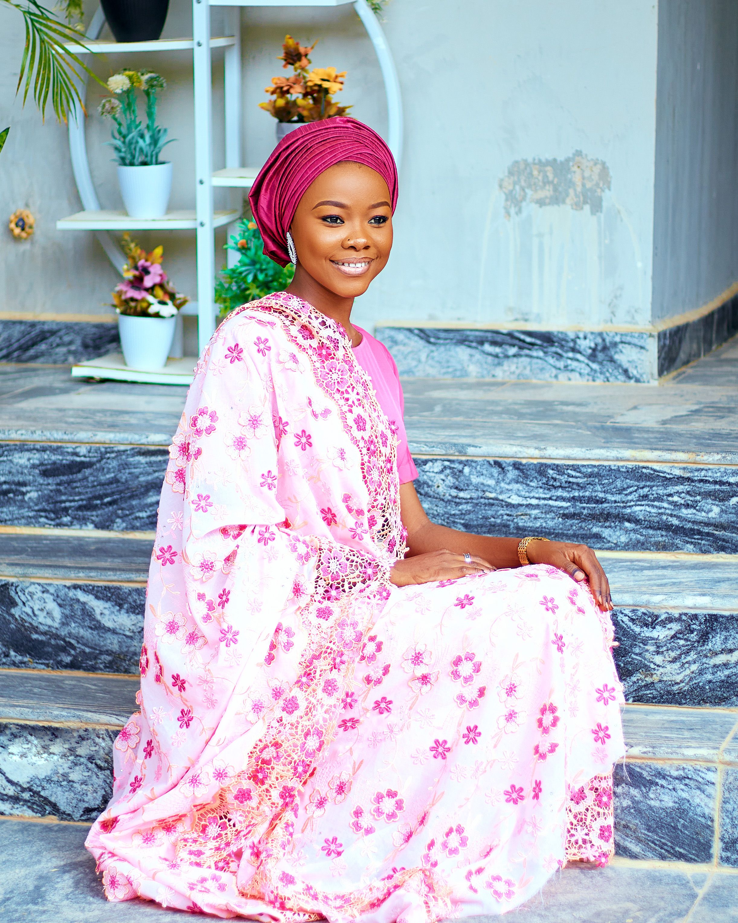 Portrait of a woman sitting on steps, wearing traditional pink attire and headscarf, smiling warmly.