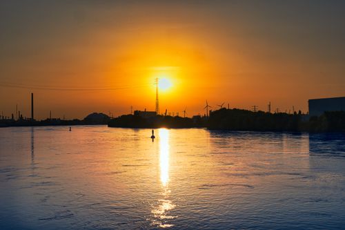 Free Beautiful sunset casting reflections over industrial landscape by river. Stock Photo