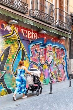 A woman strolls past colorful graffiti in a vibrant Madrid neighborhood, capturing urban life.