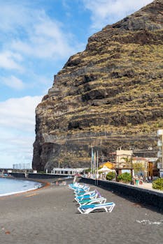 Relaxing beach view at Playa de la Arena, Canary Islands with stunning cliffs and sun loungers.