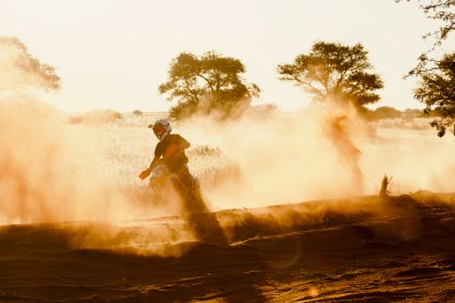 Free Two dirt bikers race on a dusty track highlighted by the warm glow of sunset. Stock Photo