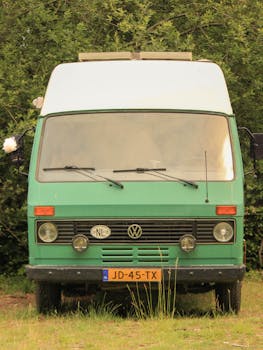 Front view of classic green Volkswagen van parked in a lush natural landscape.