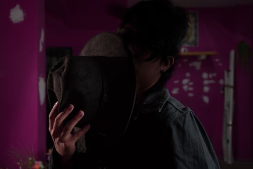 Free Silhouette of a person holding a hat in a dimly lit room with purple walls. Stock Photo