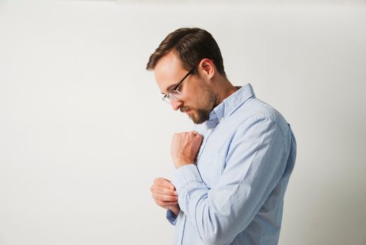 Businessman adjusting cufflinks on a white backdrop. Professional attire and thoughtful expression.