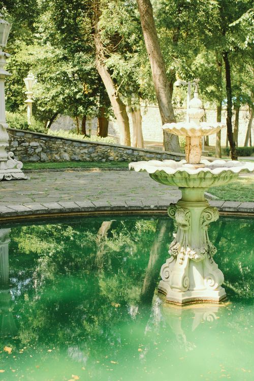 Free A classic fountain sits in a tranquil park surrounded by lush trees. Stock Photo