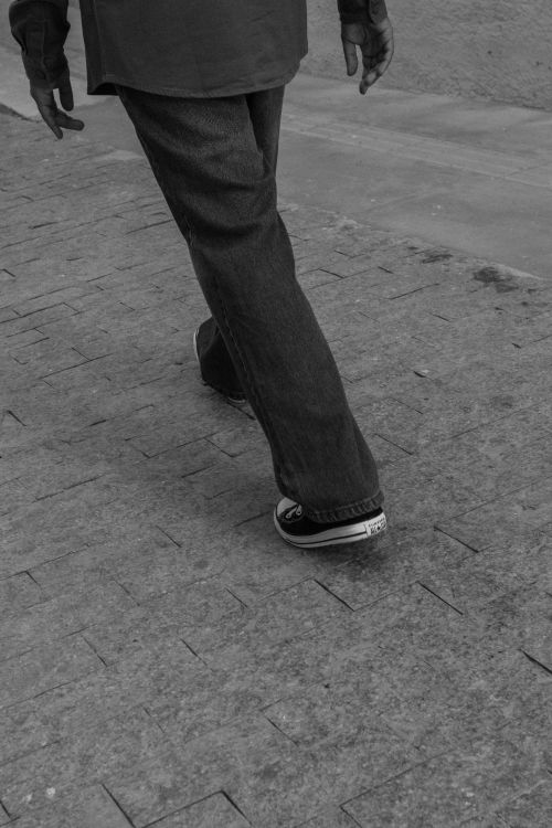 Free Black and white photo of a person walking on a tiled street, showcasing urban style. Stock Photo