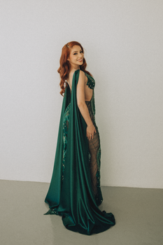 Stylish woman in an intricate green gown posing gracefully indoors.