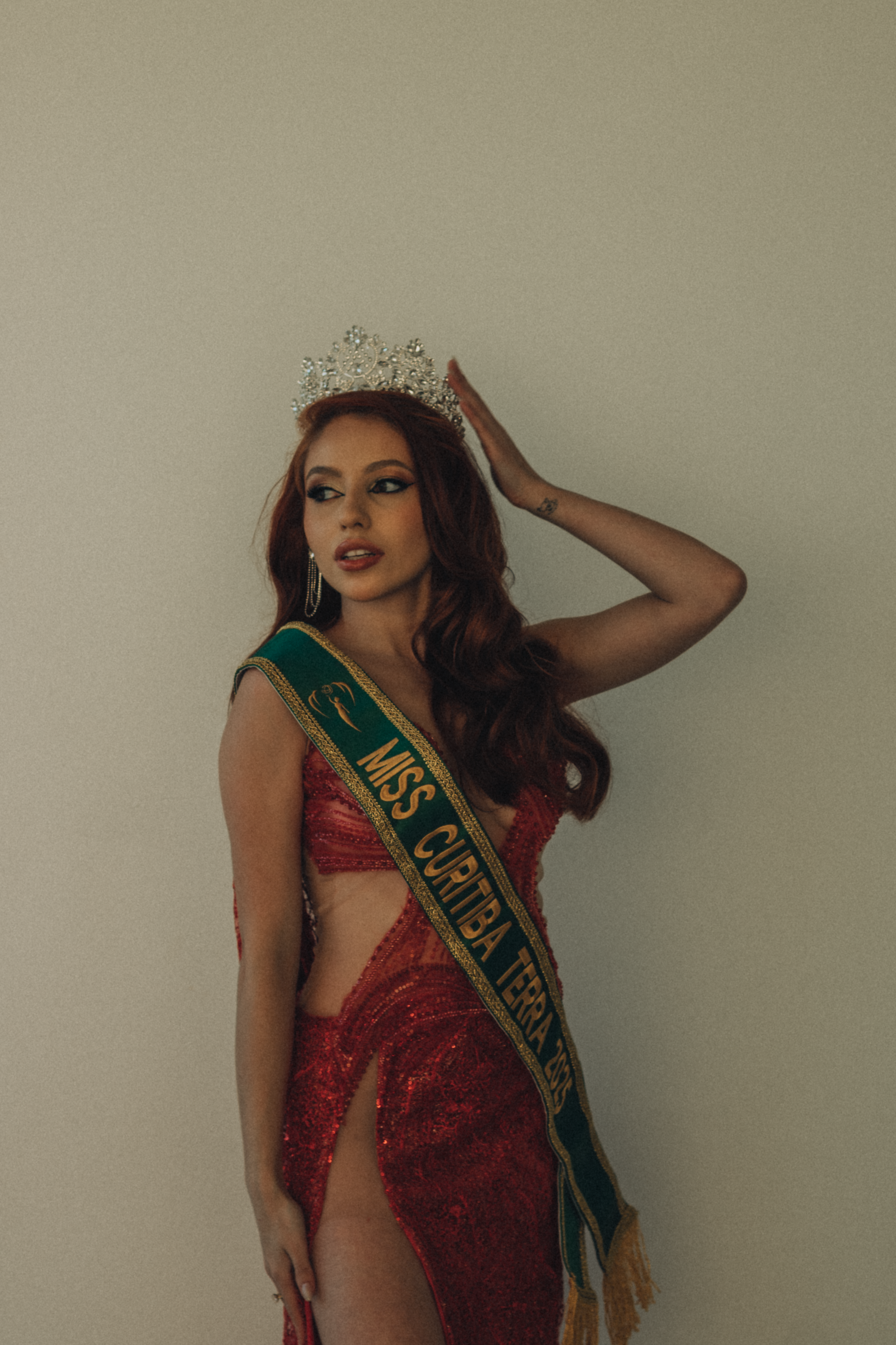 Miss beauty pageant winner wearing a crown and sash, posing elegantly in a red sequin gown.