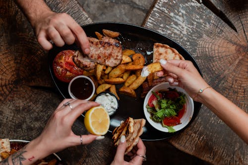 Free Several people sharing a Mediterranean meal with grilled meats, roasted vegetables, and fresh salad. Stock Photo