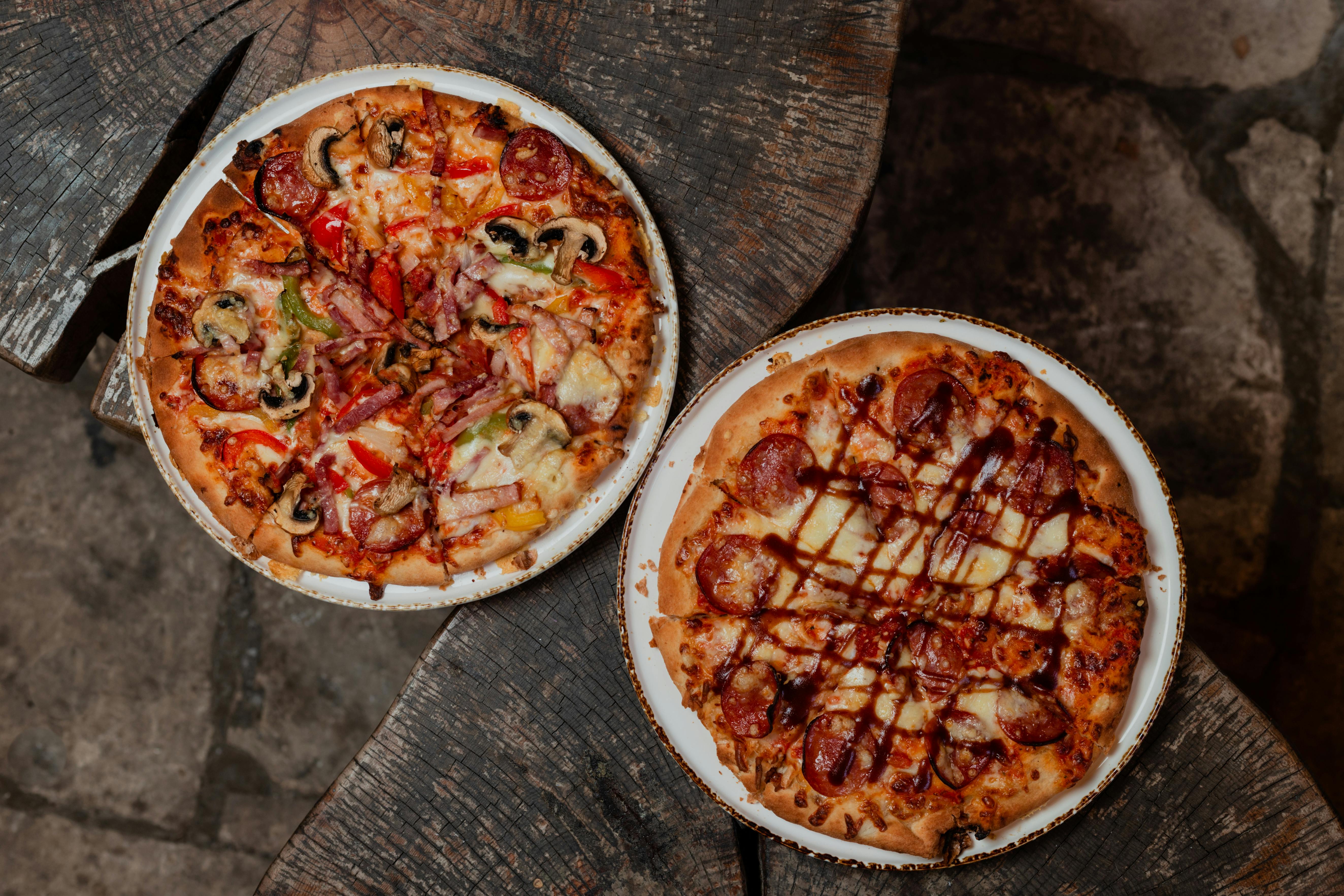 Free Overhead view of two pizzas with various toppings on rustic wooden table, ideal for food advertising Stock Photo