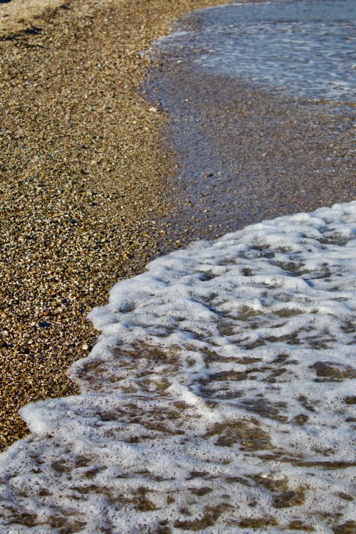 Free Rippled waves meet pebbly shore under clear skies, showcasing serene coastal beauty. Stock Photo